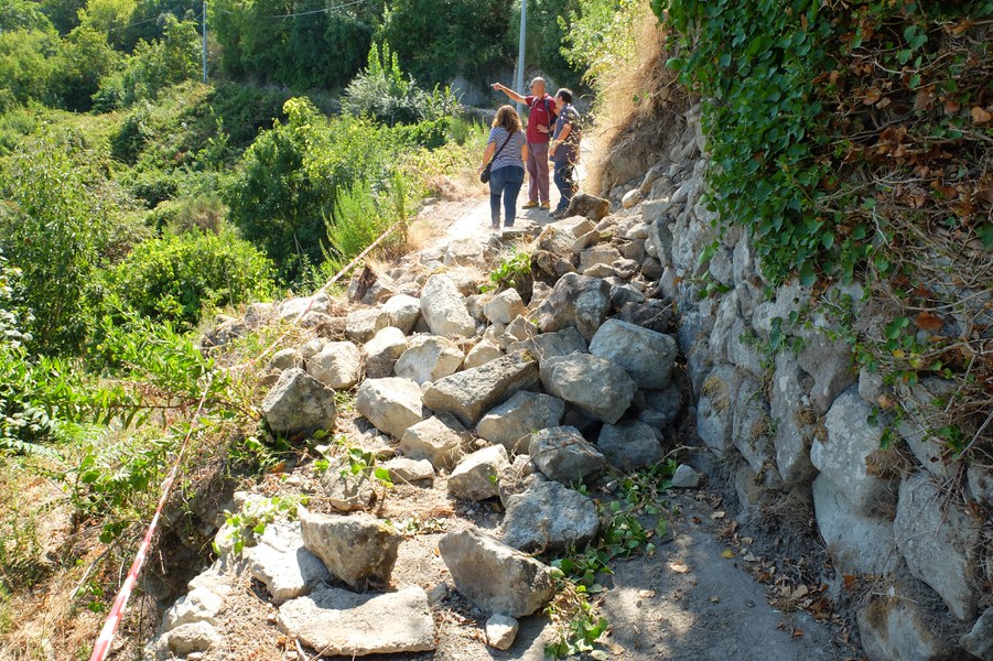 Tratto di muro a secco crollato; le pietre bloccano la strada che conduce ad alcune abitazioni